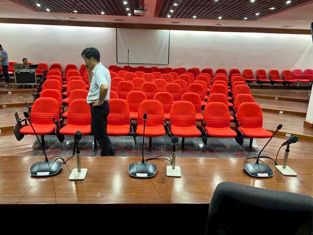 Hội trường ghế đỏ lắp đặt âm thanh và micro hội nghị trên bàn chủ tọa
